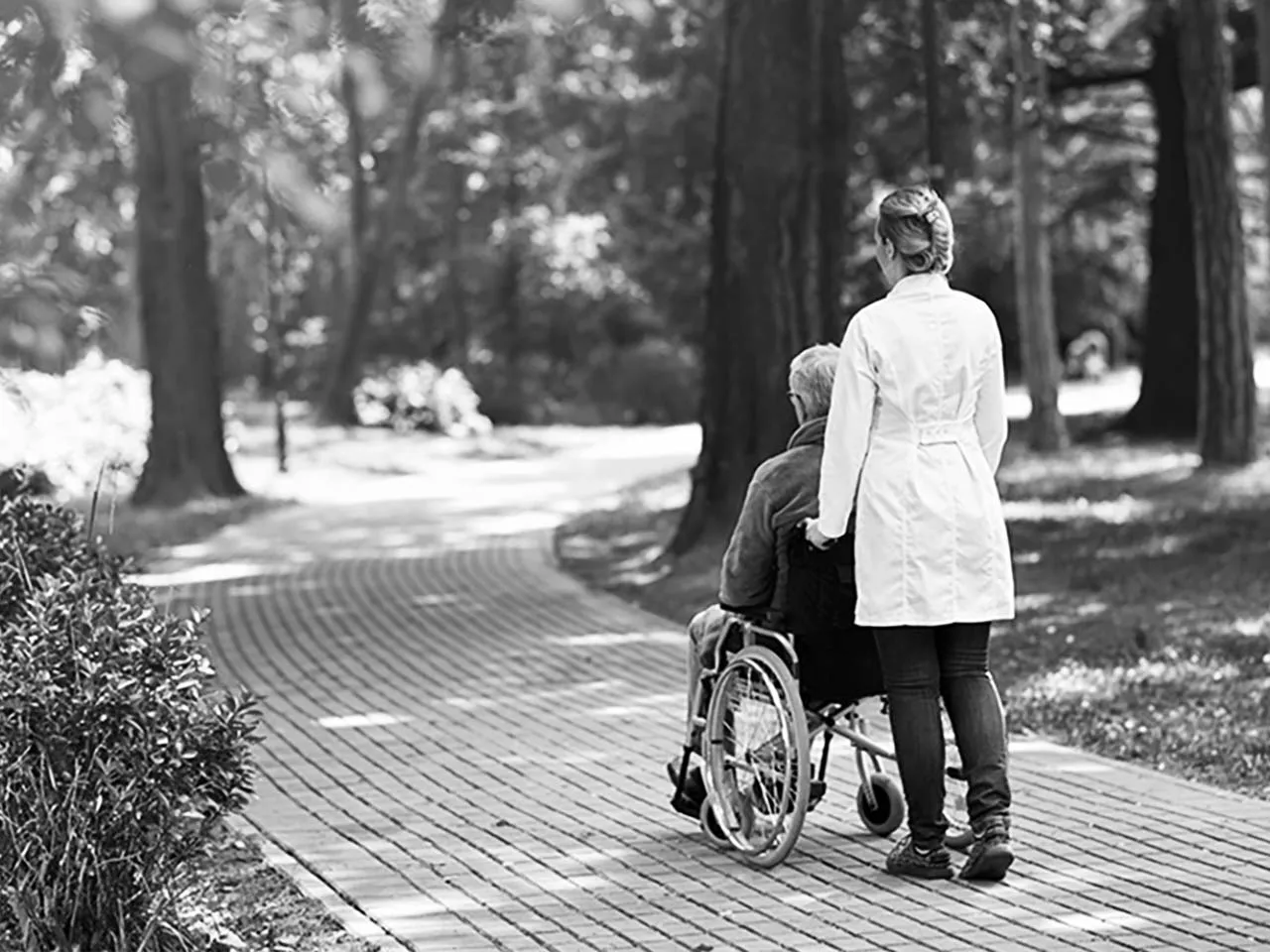 Pflegerin begleitet einen Mann im Rollstuhl durch den Park